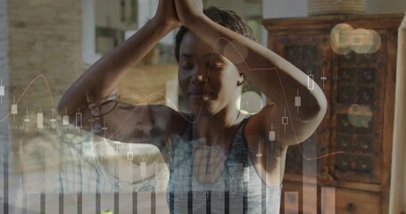 Woman practicing yoga in living room, arm raise initiating meditation amid translucent stock charts