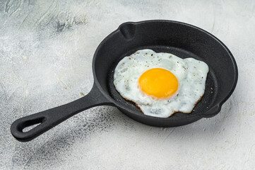 Hot frying egg in cast iron pan, glowing yolk and white contrast on bright background. Classic brunch concept with simple rustic styling.