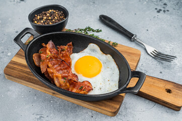 Fried egg with crisp bacon served in black skillet on stone backdrop, flavorful morning meal ideal for keto, brunch and food styling.