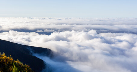Majestic clouds over mountains in Madeira, Portugal. Serene misty landscape with foggy peaks. Scenic view of nature's beauty under a clear sky.
