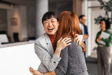 Businesswomen Joyfully Embrace During a Professional Office Setting Gathering