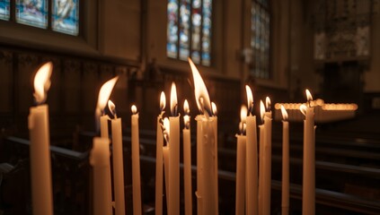 Glowing cluster of tall taper candles resting on metal rack inside chapel, casting warm light