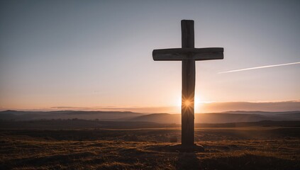 Standing weathered wooden cross casting silhouette against low sun on grass hill, rolling hills