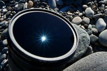 Camera Lens on Pebble Beach with Sun Reflection and Rays
