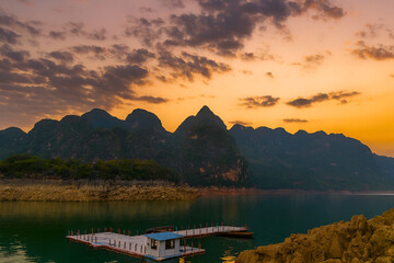 Scenic sunset landscape featuring a calm lake, floating dock, and rugged mountain range.