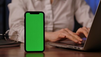 Smartphone with green screen beside a laptop in use