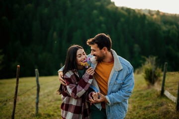 Happy couple embracing outdoors, woman holding wildflowers