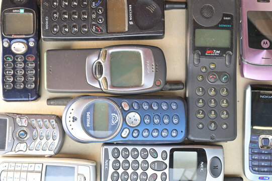 Top-down photo showing a diverse assortment of vintage mobile phones from the 1990s and early 2000s. Different models, brands, colors, and keypads are arranged closely together