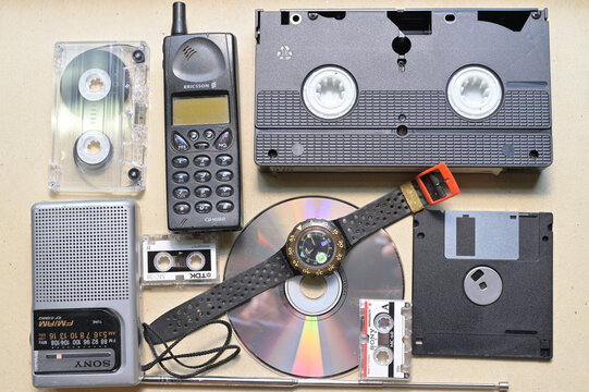  nostalgic assortment of vintage technology and media formats from 1980s and 1990s  includes mobile phone,VHS audio micro cassette, floppy disk,  portable radio, CD/DVD, watch