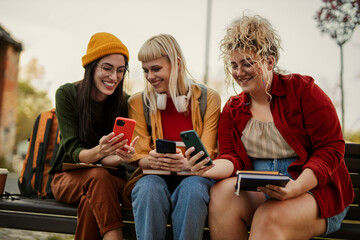 Young women friends sharing content on smartphones outdoors