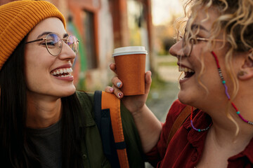 Happy young women friends laughing while drinking coffee