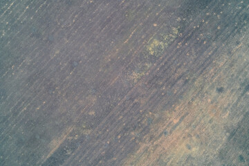 Dark grey agricultural field texture with diagonal tillage lines and small crater spots. Minimalist ground pattern - Top-down aerial view