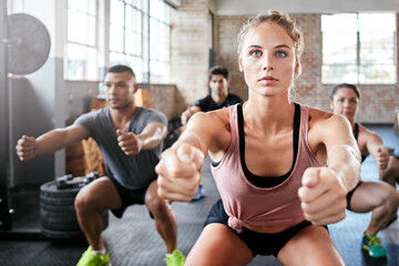 Naklejka premium Exercise, squat and woman in gym with instructor for training, wellness and challenge or fitness. Health club, personal trainer and group of people with serious, bodybuilding workout or core strength