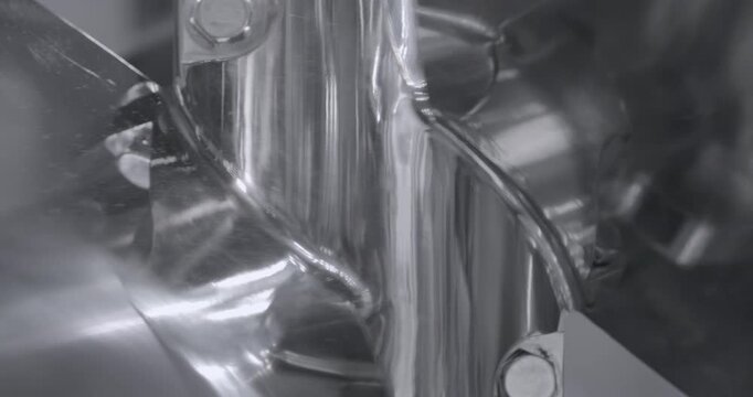 The chrome-plated steel impeller rotates, producing shifting reflections across its polished surfaces. Close up shot, abstract metal background.