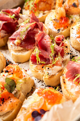 A vibrant, close-up photo of various canapés or bruschetta appetizers topped with ingredients like cured meat, salmon, and caviar on toasted bread