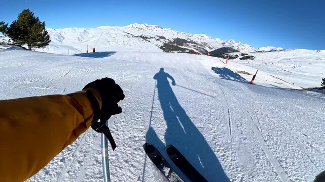 First person view of skiing downhill on a sunny day at a ski resort
