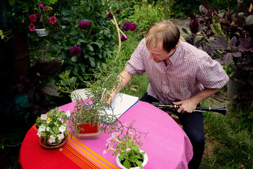 Creative man composing music outdoors, holding a clarinet and writing at a pink-covered table in a...