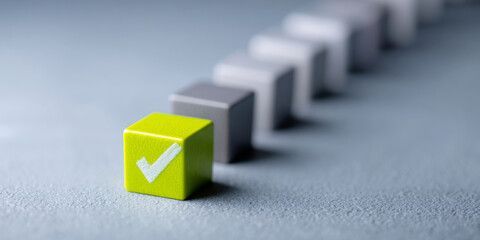 Close-up of a green cube with a white check mark standing out in front of a blurred row of gray cubes on a textured surface