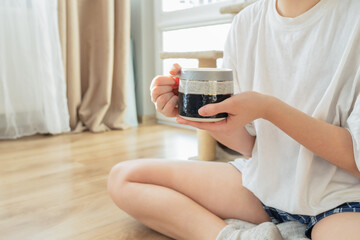 Minimalist morning moment at home: a young person sitting on the floor and holding a ceramic mug with both hands. Soft natural light, cozy atmosphere, relaxation and mindfulness concept.
