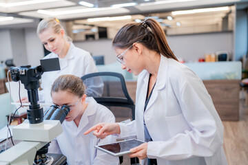 Researchers collaborate in a laboratory setting to analyze samples using a microscope and tablet