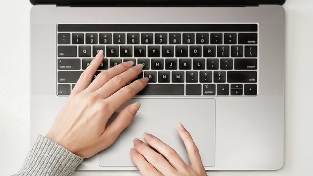 Close-up of a female hands on a laptop keyboard and touchpad browsing social networks, searching, and viewing online stores and marketplaces, modern internet usage concept.