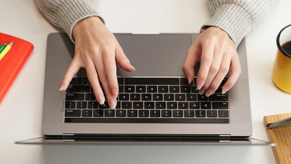 Top view of woman's hands typing on laptop keyboard, representing work, AI prompt, research, social networks, and remote education in a modern workspace.