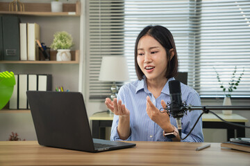 Asian female content creator adjusting her microphone while looking at a laptop in a home studio