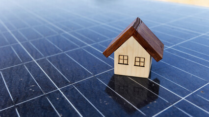 Small wooden house model placed on blue solar panel surface.