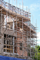 Konzept Wohnungsbau und Neubau: Blick auf die Baustelle eines Gebäude Rohbaus, komplett eingerüstet und abgesichert - Hochformat