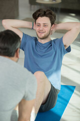 Obraz premium young man helping his friend to do abdominal crunches