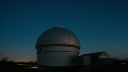 Towering observatory dome glowing at observatory site with annex, trees, ground lights, star trails