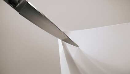 Slicing stainless-steel knife blade parting folded paper on studio table, casting sharp shadow