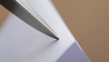 Hovering sharp metal blade tip catching light above white paper corner on pale purple studio table