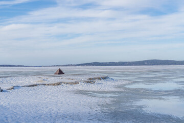 Snowy winter panorama of Lake Onega near Petrozavodsk with small pyramidal navigation marker rising from the frozen surface in Karelia, Russia.
