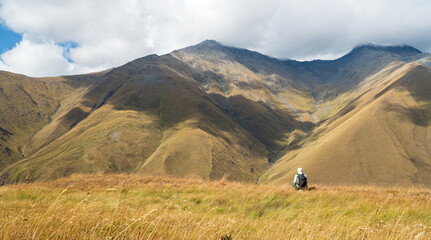 Solo hiker resting on grass while admiring the mountains near Juta Village, Georgia. Peaceful outdoor photo symbolizing mindfulness and connection to nature.