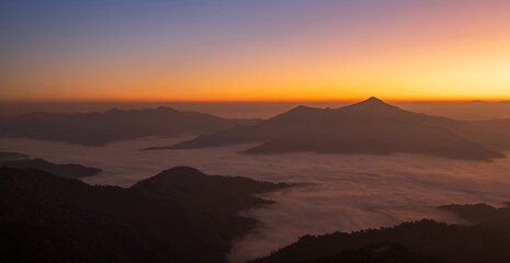 Sunrise over misty mountain range with warm orange sky and peaceful atmosphere