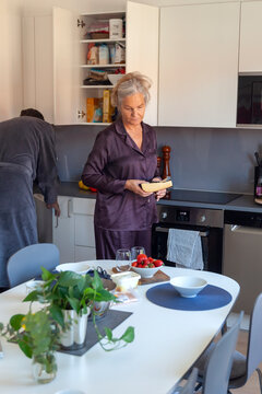 Senior woman holding cheese slice while standing in kitchen