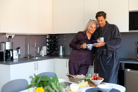 Senior couple having coffee while watching phone in kitchen at home