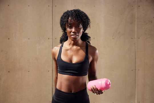 Portrait of confident female athlete holding water bottle against wall