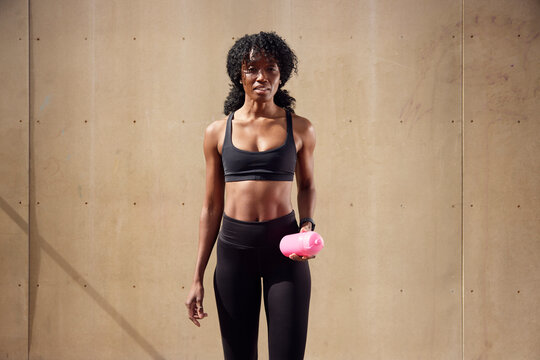 Portrait of young female athlete standing in front of wall