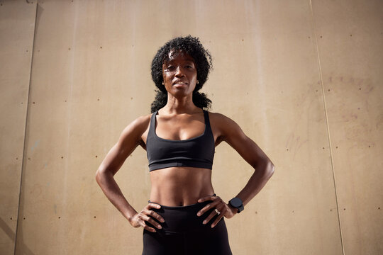 Low angle view of confident woman standing with arms akimbo against wall