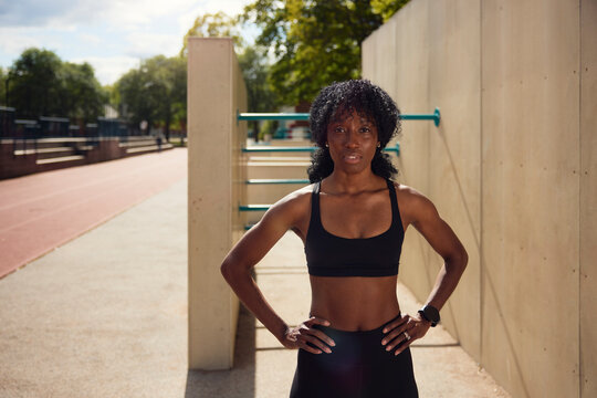 Confident young woman posing with arms akimbo at park during sunny day