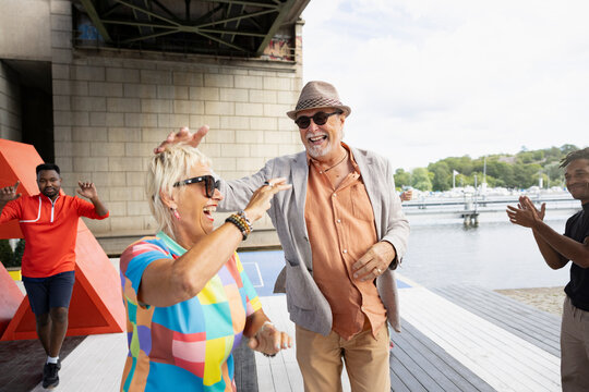 Happy mature man and woman enjoying leisure time on pier with friends