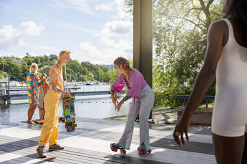 Young woman showing roller skating skills to female friend on platform at sunny day