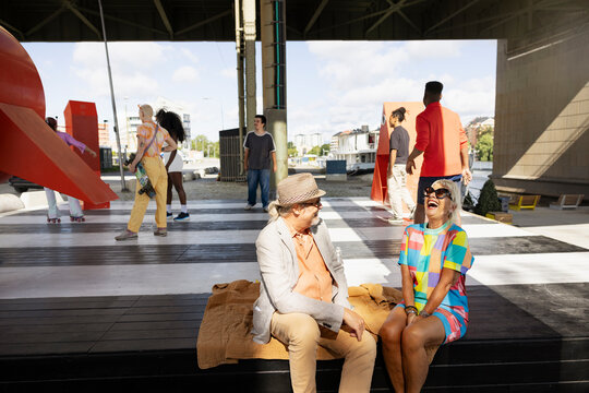 Laughing mature woman sitting with man on platform and spending leisure time