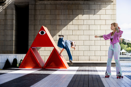 Young man practicing stunts while woman roller skating on platform at sunny day