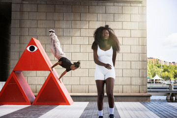 Young woman walking on platform while man balancing on red structure