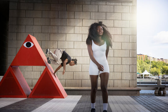 Young woman walking on platform while man doing stunts on red structure