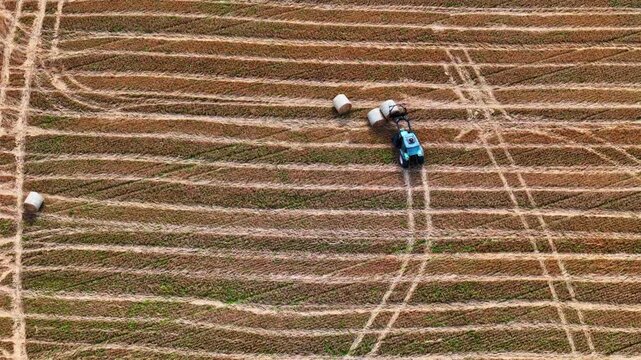 Drone video of tractor using front loader to collect hay bales from field