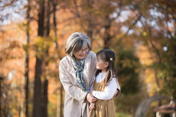 Grandmother playing in the autumn park with its red leaves, her granddaughter nestled close beside her